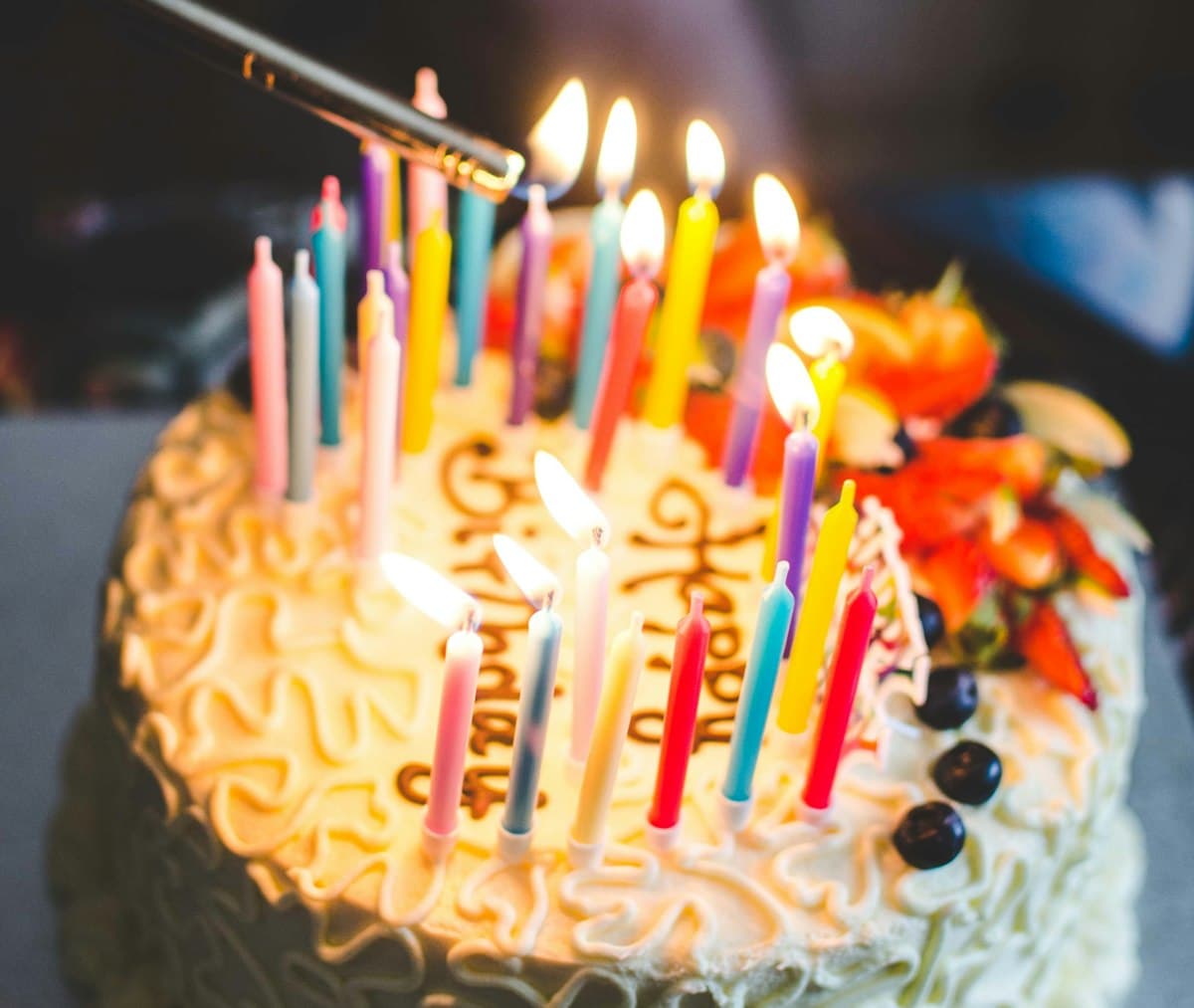 Hand lighting candles on a white-frosted birthday cake decorated with berries